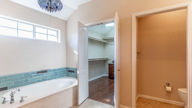 bathroom with a tub to relax in, a notable chandelier, tile patterned flooring, toilet, and lofted ceiling