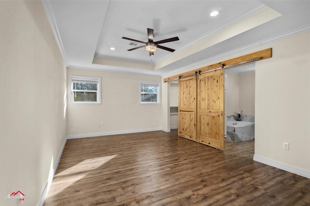 unfurnished bedroom with a raised ceiling, dark hardwood / wood-style floors, a barn door, ceiling fan, and ornamental molding