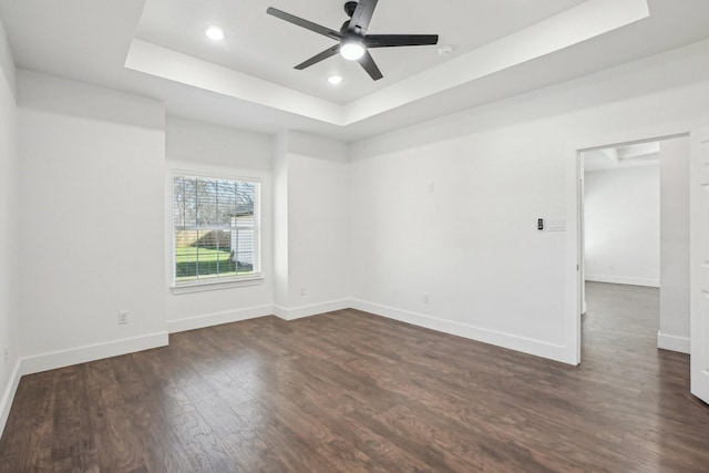 spare room with a raised ceiling, dark wood-type flooring, and ceiling fan