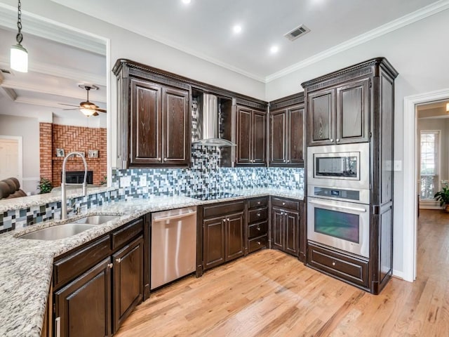 kitchen with sink, wall chimney exhaust hood, decorative light fixtures, decorative backsplash, and appliances with stainless steel finishes