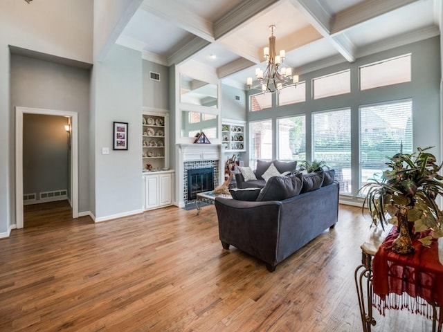 living room with a notable chandelier, built in shelves, hardwood / wood-style floors, and beamed ceiling