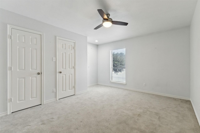 unfurnished bedroom featuring ceiling fan, two closets, and light carpet