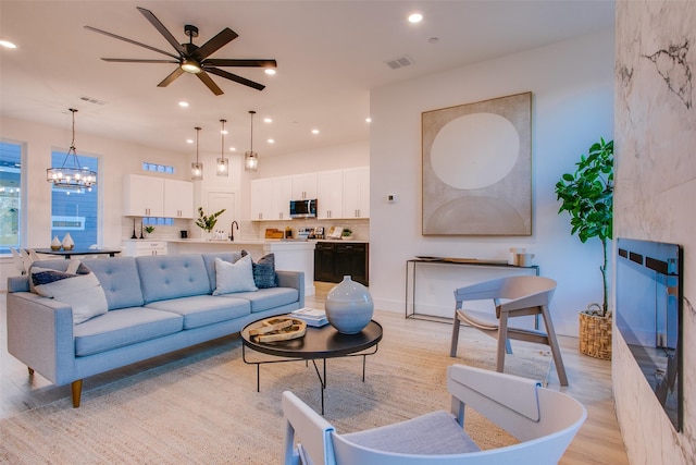 living room featuring ceiling fan with notable chandelier, light hardwood / wood-style floors, and sink