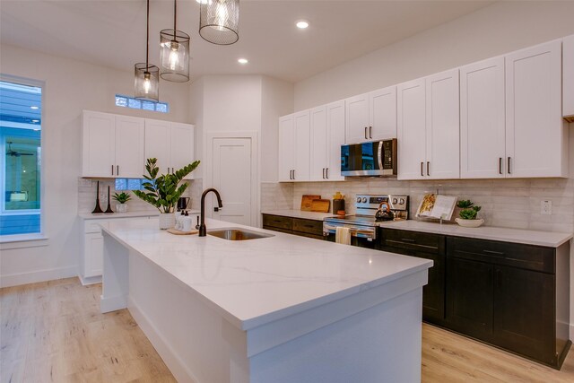 kitchen featuring appliances with stainless steel finishes, white cabinetry, a kitchen island with sink, and sink