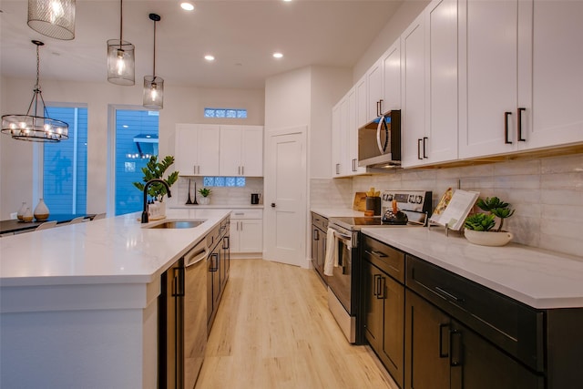 kitchen with stainless steel appliances, a kitchen island with sink, sink, pendant lighting, and white cabinetry