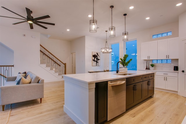 kitchen featuring pendant lighting, ceiling fan with notable chandelier, sink, stainless steel dishwasher, and an island with sink