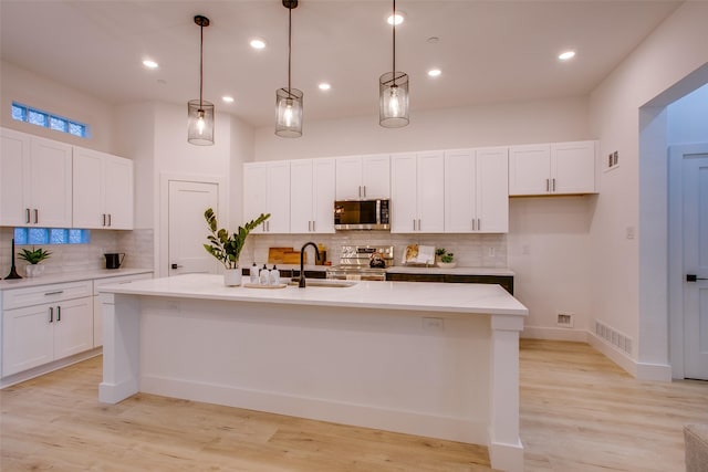 kitchen featuring stainless steel appliances, a kitchen island with sink, sink, decorative light fixtures, and white cabinetry