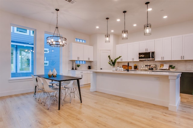 kitchen featuring decorative backsplash, stainless steel appliances, decorative light fixtures, white cabinets, and an island with sink