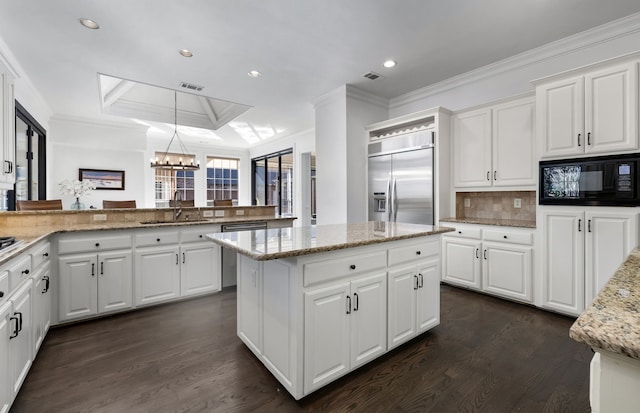 kitchen featuring built in appliances, decorative light fixtures, white cabinetry, and sink