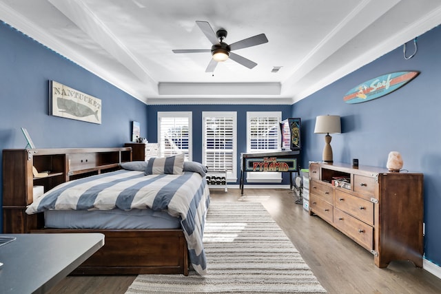 bedroom featuring ceiling fan, light hardwood / wood-style floors, a raised ceiling, and crown molding