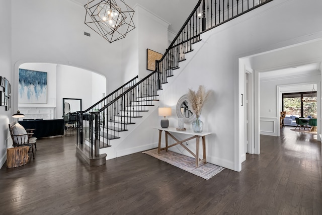 entryway with dark hardwood / wood-style flooring, a towering ceiling, crown molding, and a chandelier