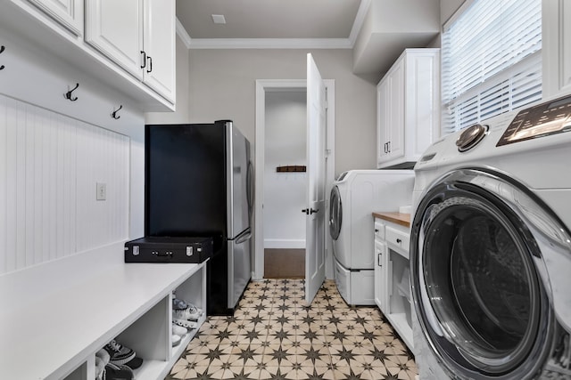 clothes washing area featuring washing machine and clothes dryer, crown molding, and cabinets