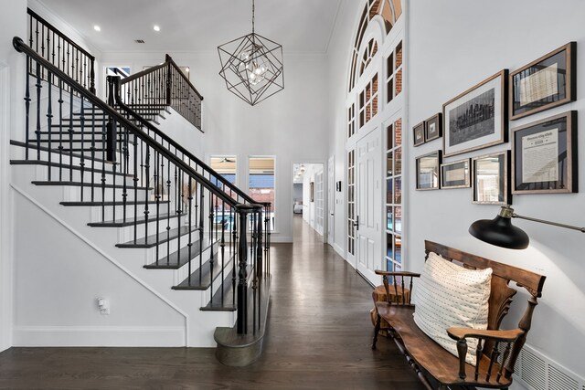 staircase with french doors, crown molding, wood-type flooring, an inviting chandelier, and a high ceiling