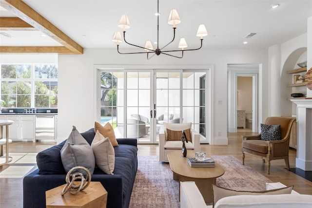 living room featuring french doors, sink, beam ceiling, light hardwood / wood-style flooring, and a notable chandelier