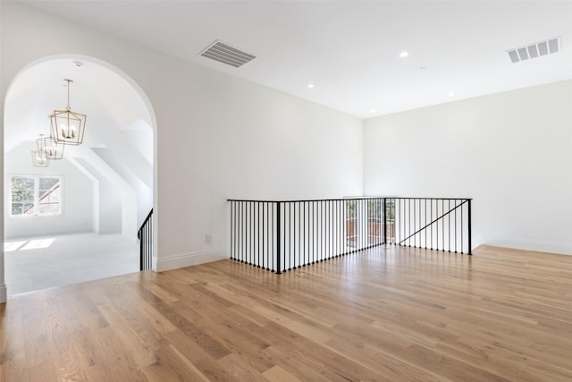 unfurnished room with lofted ceiling, a notable chandelier, and light wood-type flooring