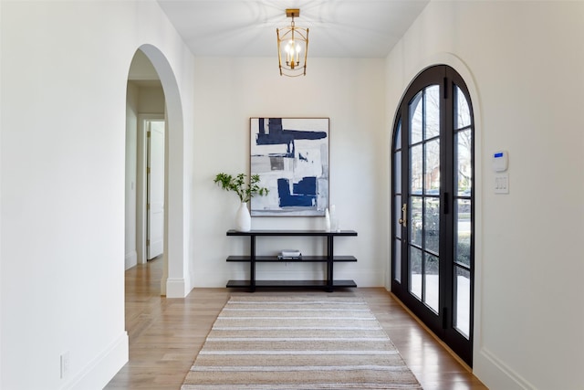 interior space featuring french doors, light wood-type flooring, and a notable chandelier