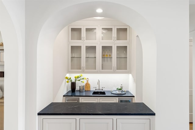 bar featuring dark stone countertops, white cabinetry, and sink