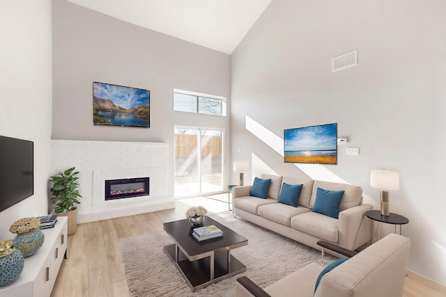 living room featuring light wood-type flooring, a towering ceiling, and a brick fireplace