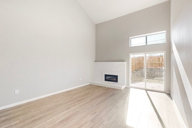 unfurnished living room featuring a fireplace, light hardwood / wood-style floors, and high vaulted ceiling