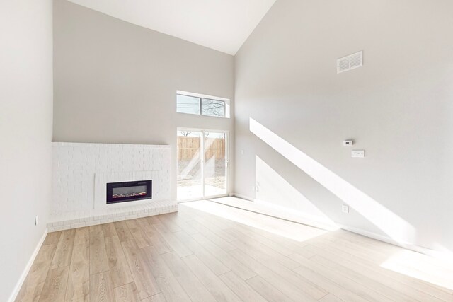 unfurnished living room with a fireplace, light hardwood / wood-style floors, and high vaulted ceiling