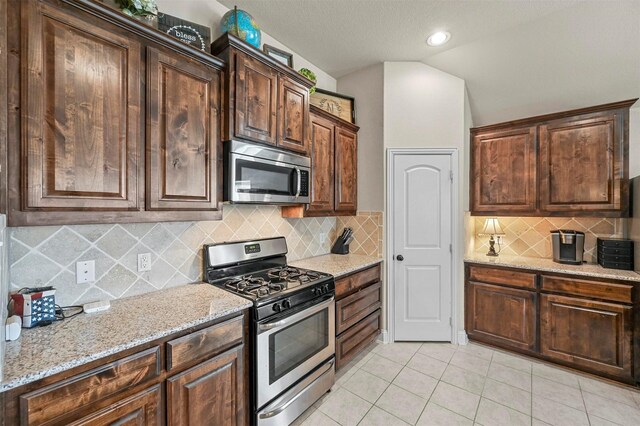 kitchen with light stone countertops, tasteful backsplash, stainless steel appliances, vaulted ceiling, and light tile patterned flooring