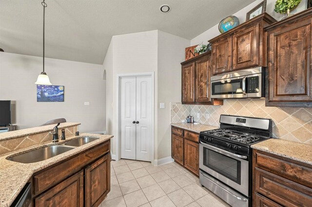 kitchen with appliances with stainless steel finishes, tasteful backsplash, sink, decorative light fixtures, and light tile patterned flooring