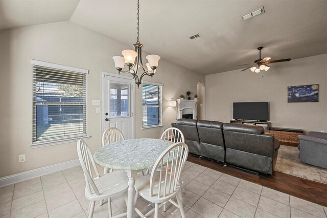 tiled dining room featuring ceiling fan with notable chandelier and lofted ceiling