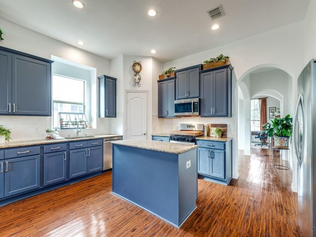 kitchen featuring appliances with stainless steel finishes, a center island, dark wood-type flooring, blue cabinets, and sink