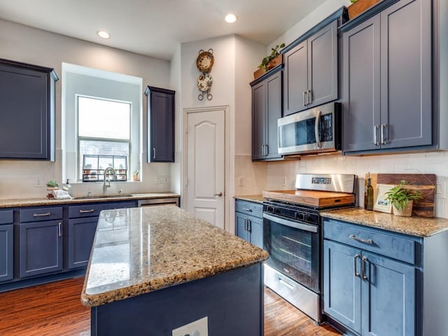 kitchen with sink, light stone counters, appliances with stainless steel finishes, dark hardwood / wood-style floors, and a kitchen island