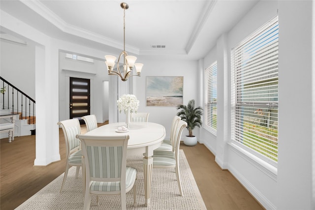 dining space featuring a raised ceiling, light wood-type flooring, an inviting chandelier, and crown molding