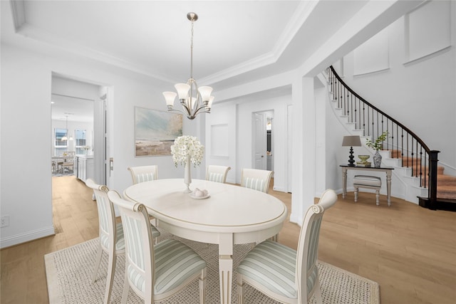 dining room featuring ornamental molding, light wood-type flooring, a tray ceiling, and a notable chandelier