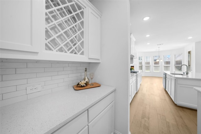 kitchen with white cabinetry, sink, tasteful backsplash, light stone counters, and pendant lighting