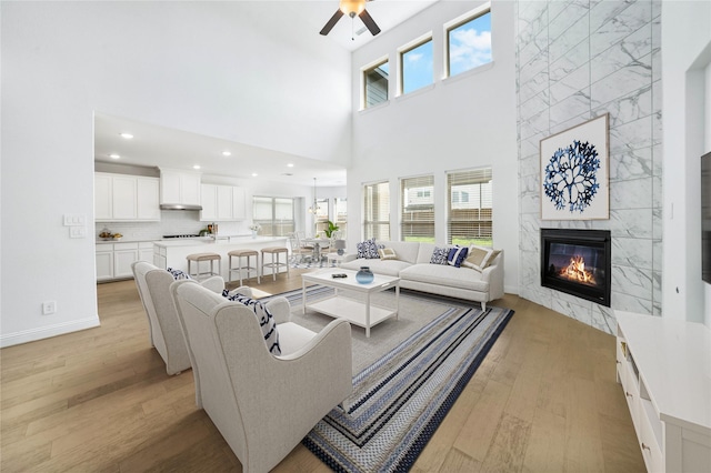 living room with ceiling fan, light hardwood / wood-style floors, a towering ceiling, and a high end fireplace