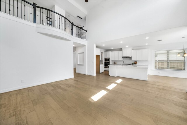 unfurnished living room with light hardwood / wood-style floors, a high ceiling, and an inviting chandelier