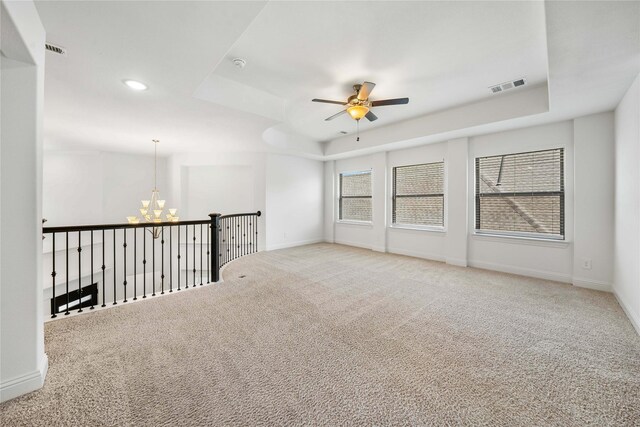 carpeted spare room featuring a tray ceiling and ceiling fan with notable chandelier