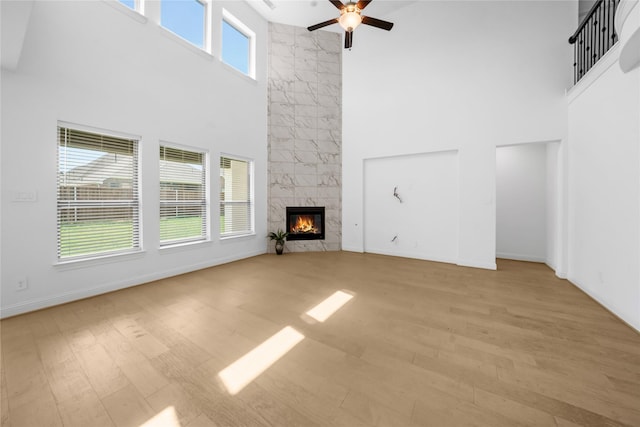 unfurnished living room featuring ceiling fan, light hardwood / wood-style floors, a towering ceiling, and a premium fireplace