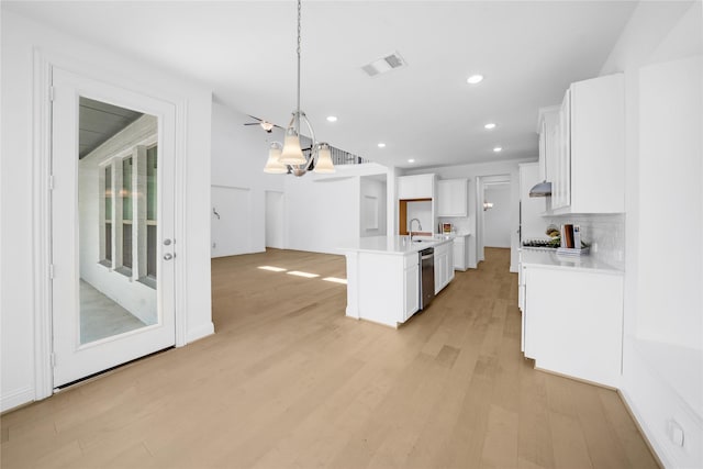 kitchen featuring sink, hanging light fixtures, stainless steel dishwasher, an island with sink, and white cabinets