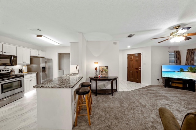 kitchen with white cabinetry, stainless steel appliances, a breakfast bar area, dark stone countertops, and sink