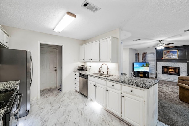 kitchen featuring stainless steel appliances, a tile fireplace, white cabinets, dark stone counters, and sink