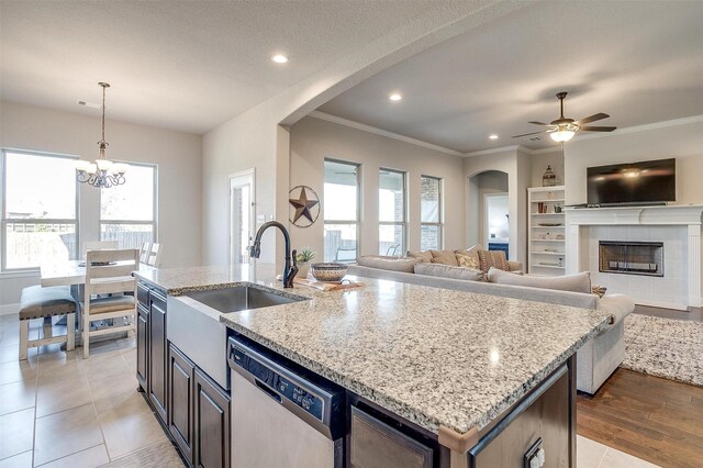 kitchen with sink, stainless steel dishwasher, an island with sink, decorative light fixtures, and light stone counters