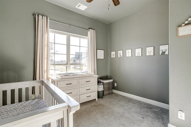 bedroom featuring a crib, light colored carpet, and ceiling fan