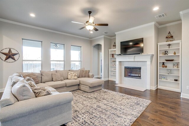 living room featuring dark hardwood / wood-style flooring, ceiling fan, crown molding, and a tiled fireplace