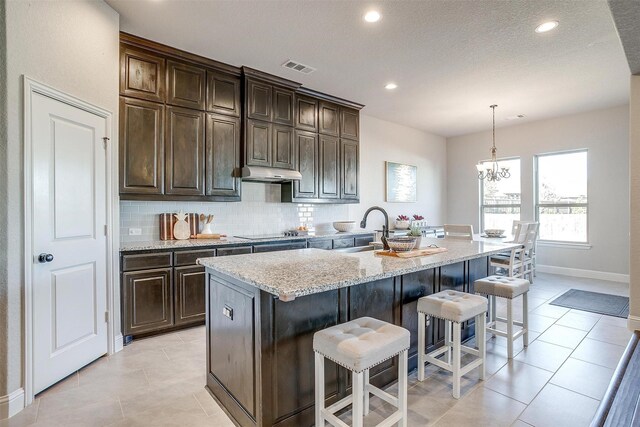 kitchen featuring dark brown cabinets, a center island with sink, and hanging light fixtures