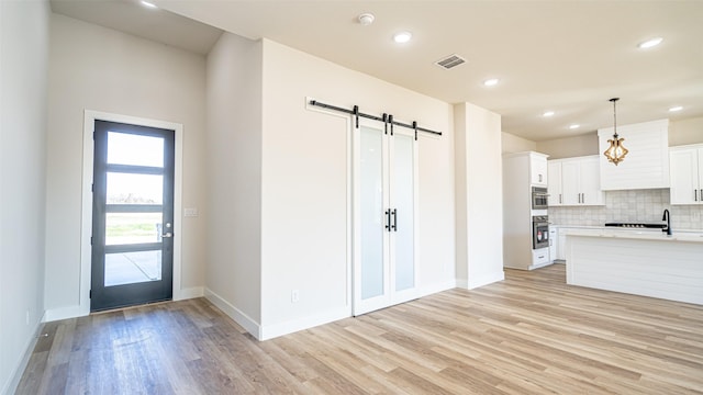 kitchen with a barn door, backsplash, oven, decorative light fixtures, and white cabinets