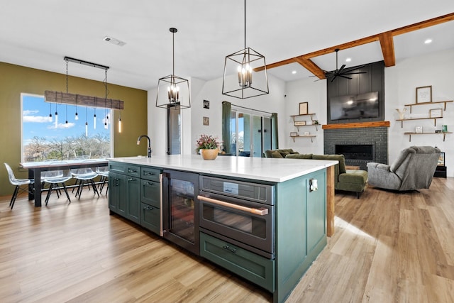 kitchen with beverage cooler, ceiling fan, decorative light fixtures, a center island with sink, and a fireplace