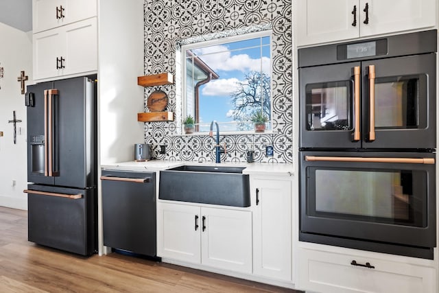 kitchen featuring dishwasher, high end refrigerator, sink, multiple ovens, and white cabinetry