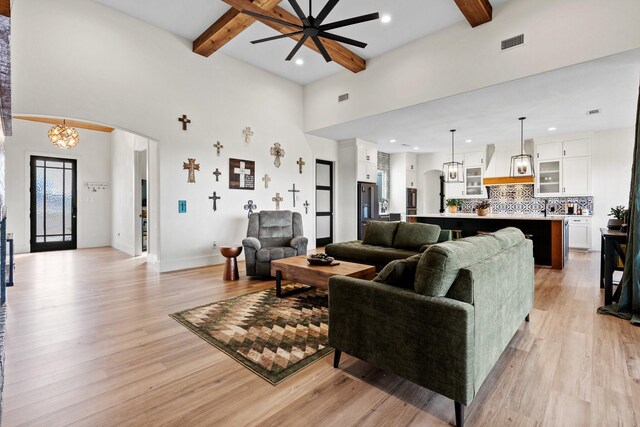 living room with beam ceiling, light hardwood / wood-style floors, and ceiling fan with notable chandelier