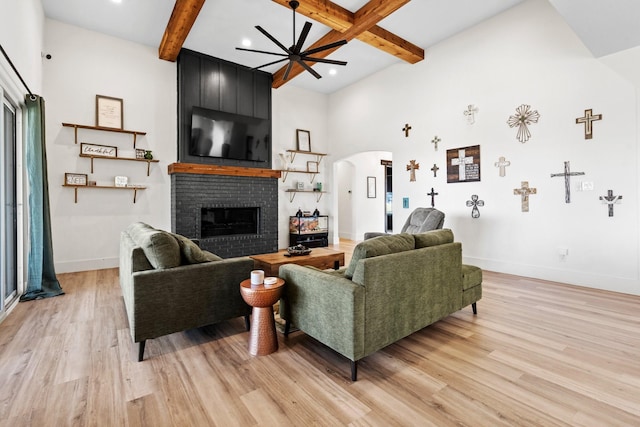 living room featuring beamed ceiling, light hardwood / wood-style flooring, a brick fireplace, and ceiling fan