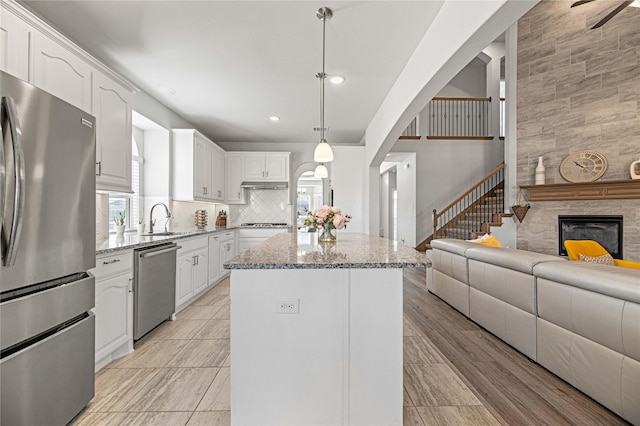 kitchen with open floor plan, appliances with stainless steel finishes, a kitchen island, and light stone countertops