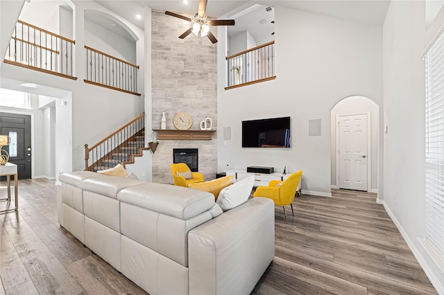 living room with a fireplace, a towering ceiling, wood finished floors, baseboards, and stairs